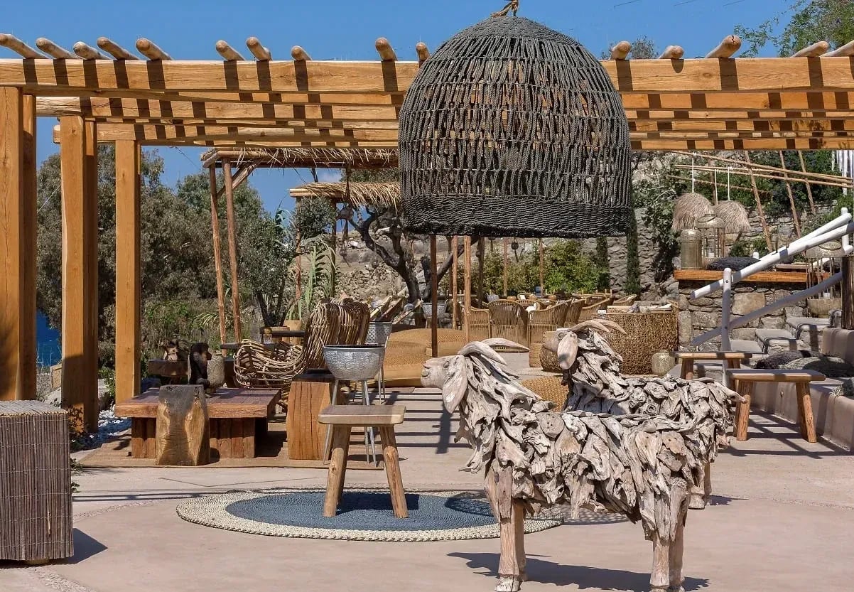 Woven pendant hanging under the timber pergola of the Garden of Mykonos bar, with driftwood sculptures below