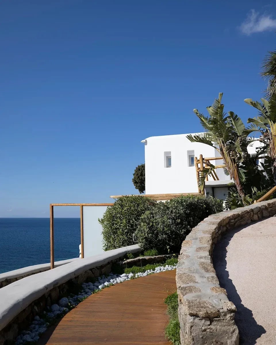 Timber walkway curving between clipped planting and a stone wall in the garden, the open sea beyond