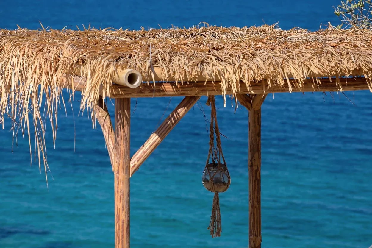 Thatched shade canopy on timber posts above the turquoise water of the bay