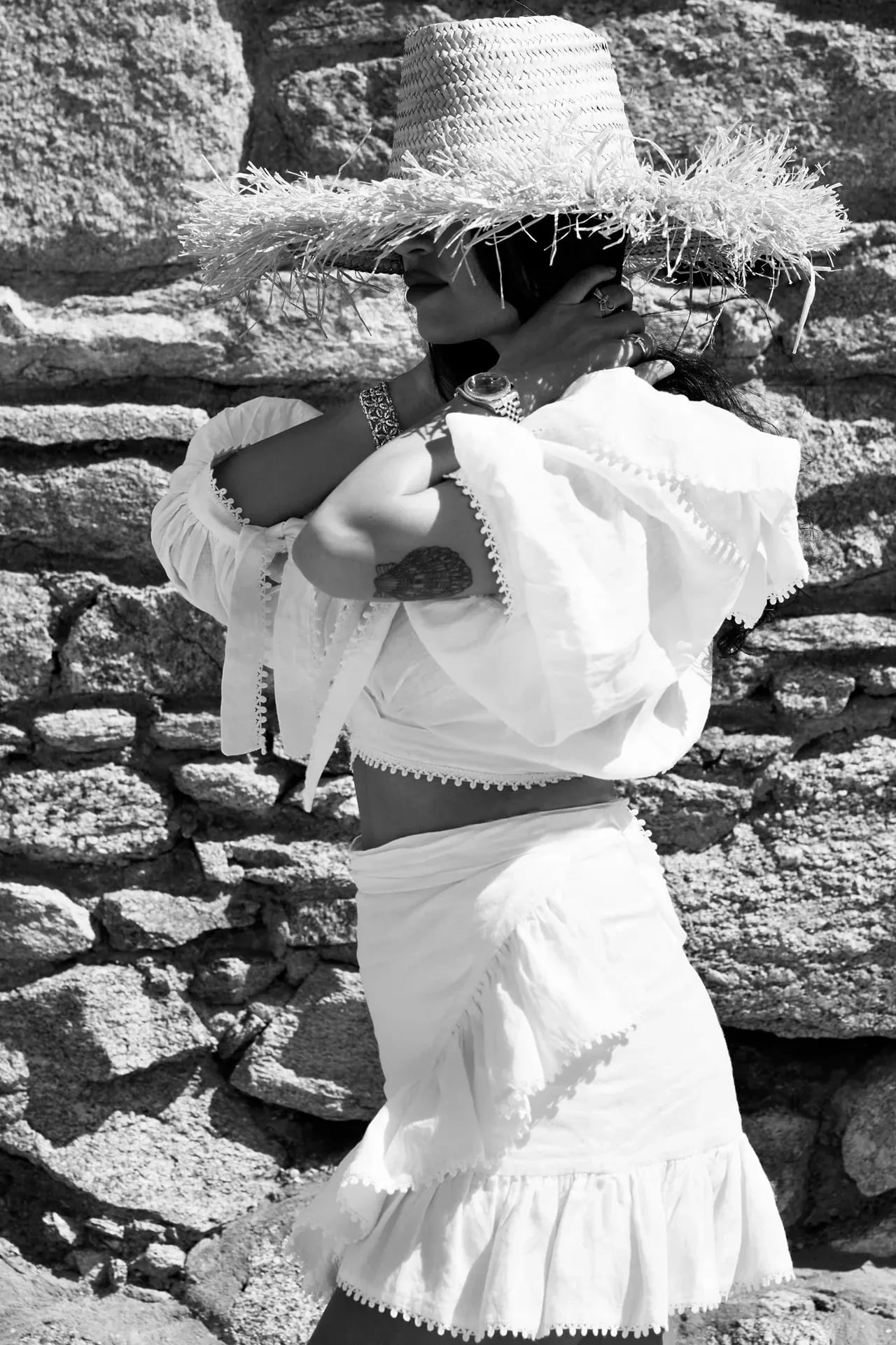 Black and white portrait of a guest in a straw hat against the dry-stone wall