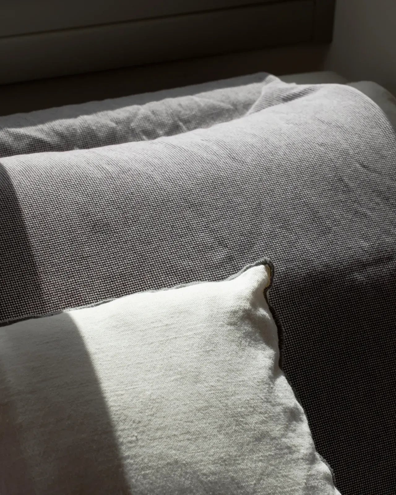 Linen cushions on a bed, lit by a shaft of afternoon sun