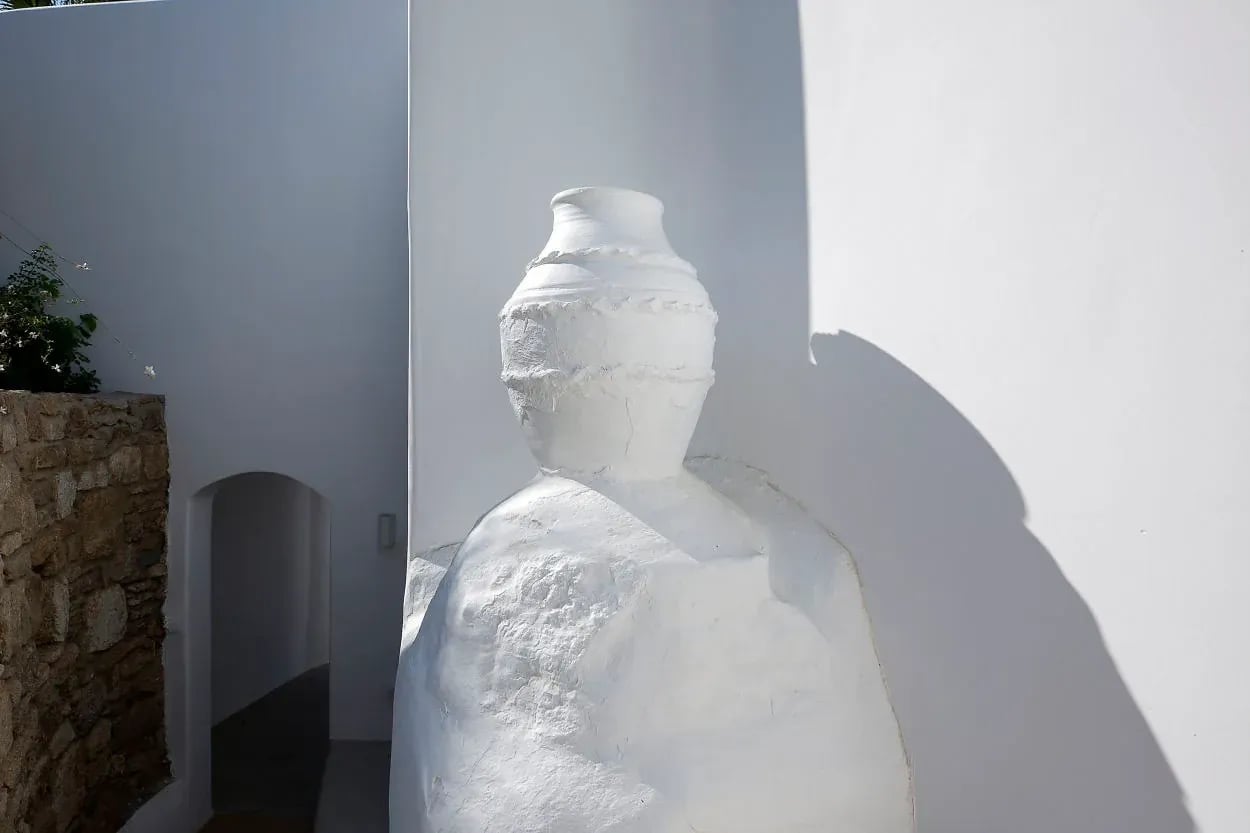 A white plaster figure standing against a whitewashed wall beside an arched passage