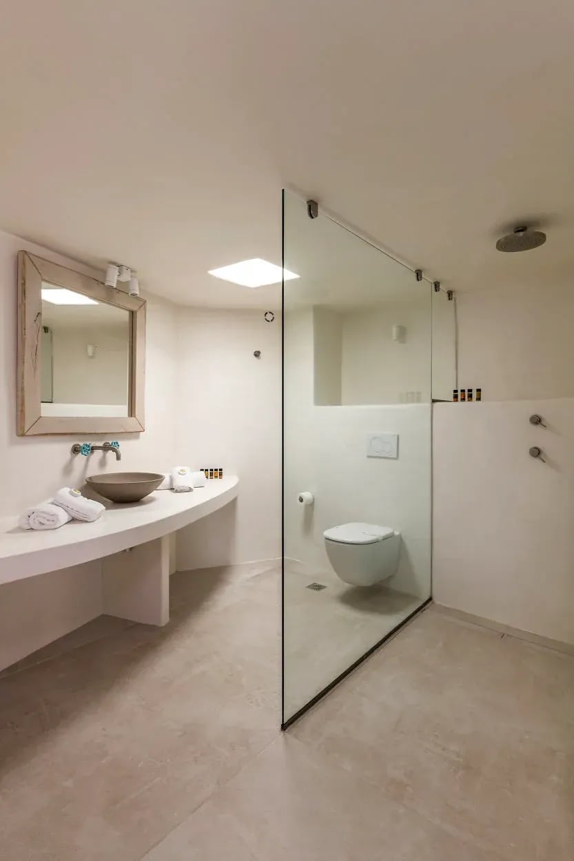 A suite bathroom with stone basin, mirror and a walk-in shower behind clear glass