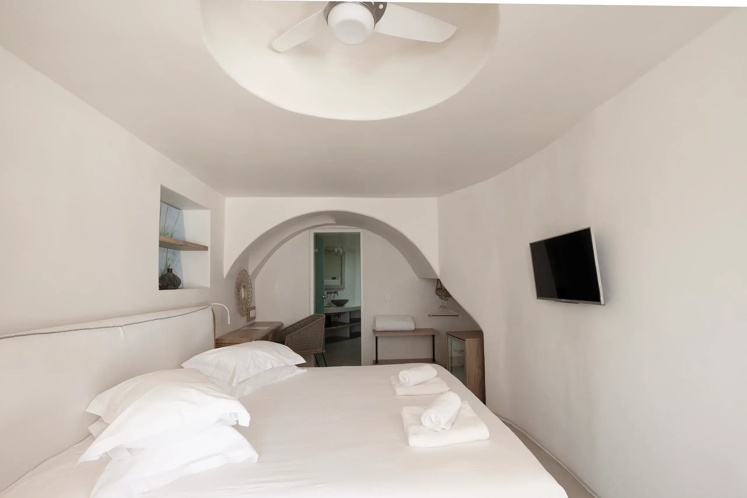 A suite bedroom under a curved plaster ceiling, with an arched opening through to the bathroom
