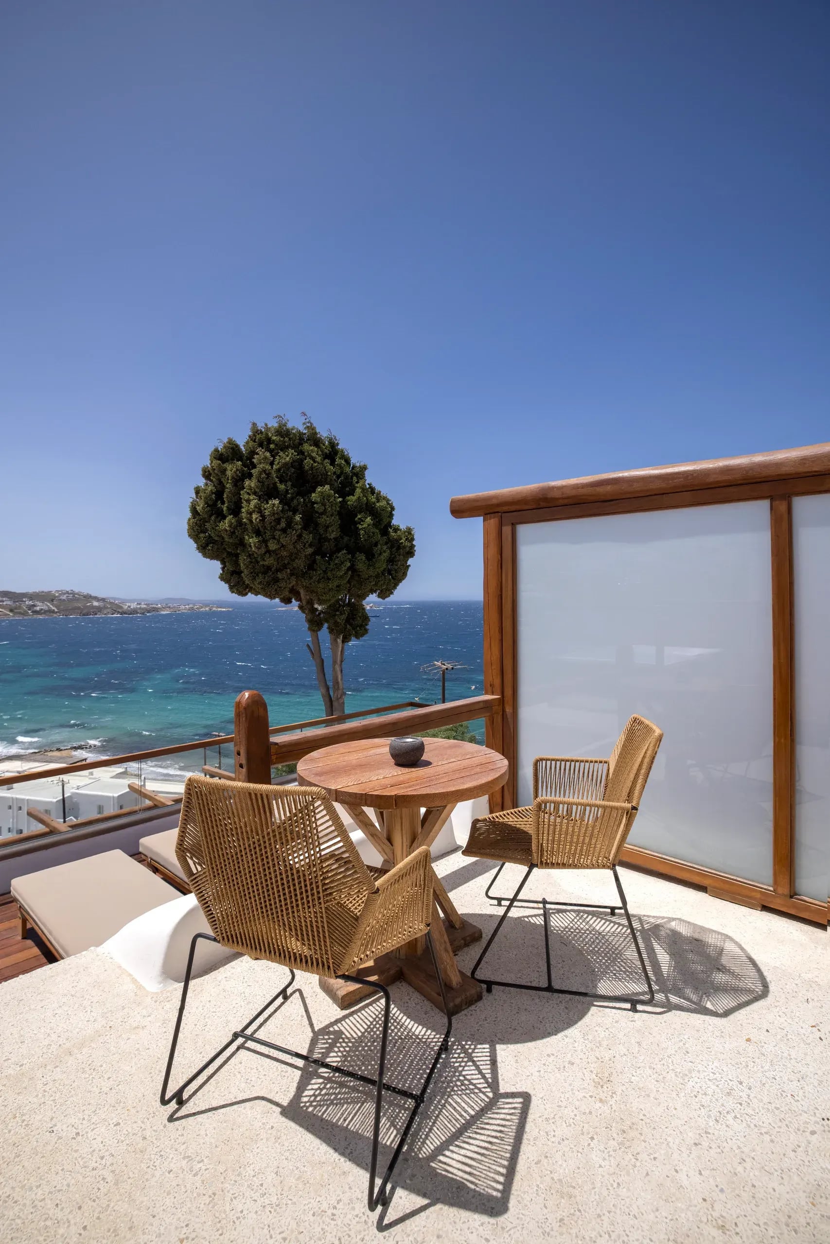 Table and chairs set on a private terrace, with a tree and the open sea beyond