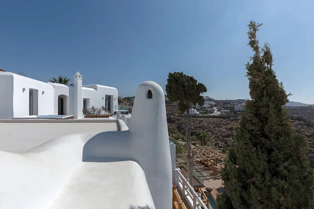 Whitewashed Cycladic volumes and a chimney against a cypress and the open hillside