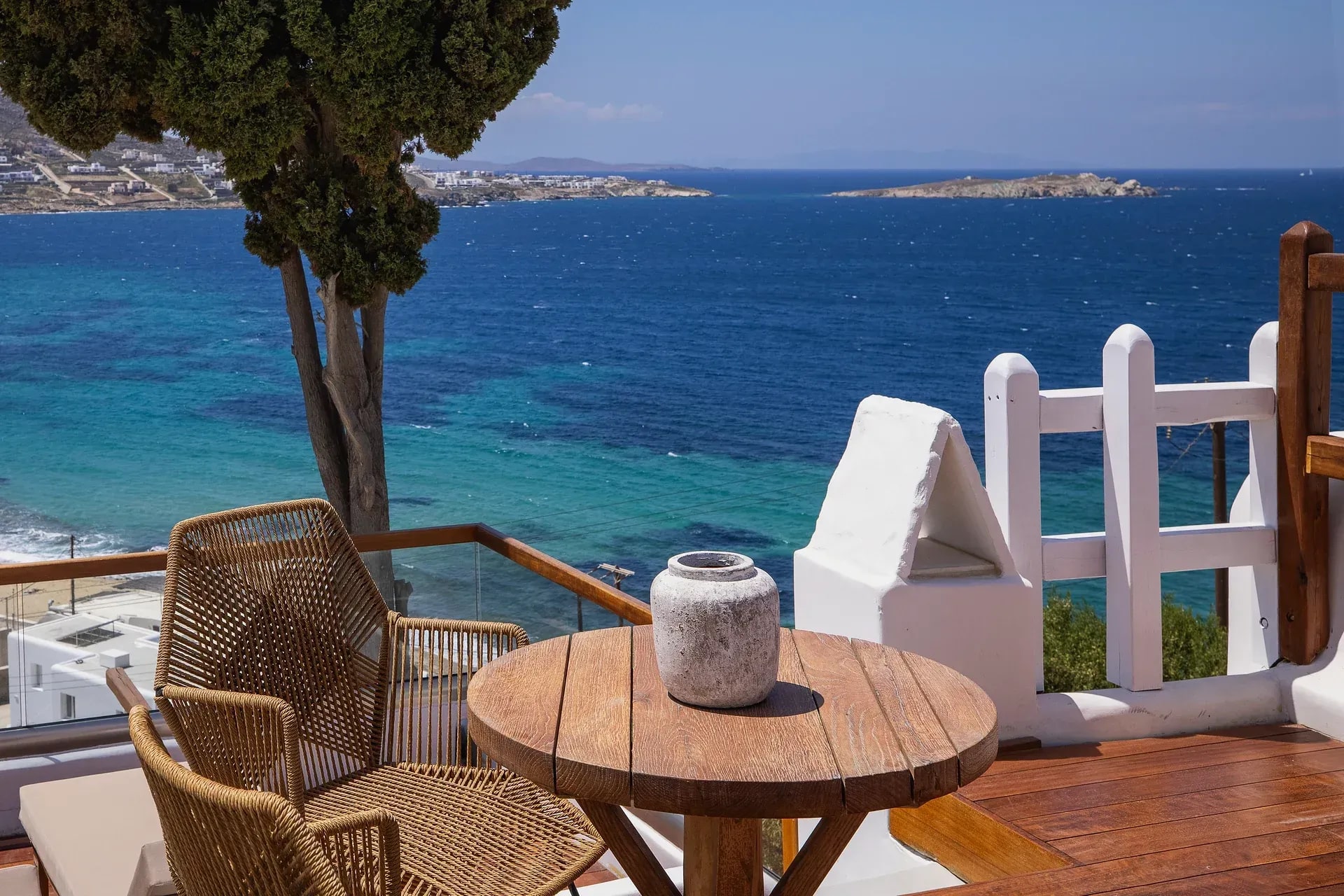 Terrace table and chairs framed by a tree above the turquoise water