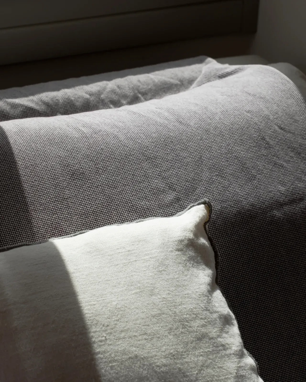 Linen cushions on a bed, lit by a shaft of afternoon sun