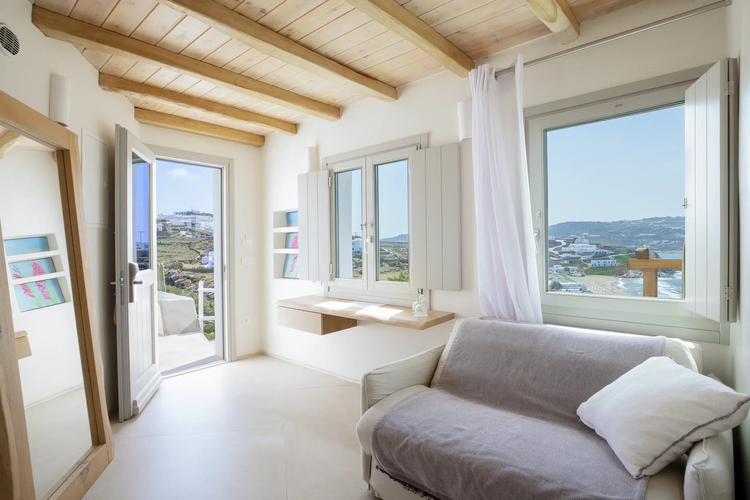 Living area of a Legacy Mykonos suite, with timber beam ceiling and sea-facing windows