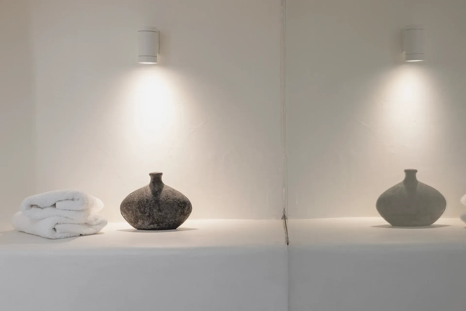 Folded towels and ceramic vessels in a lit wall niche