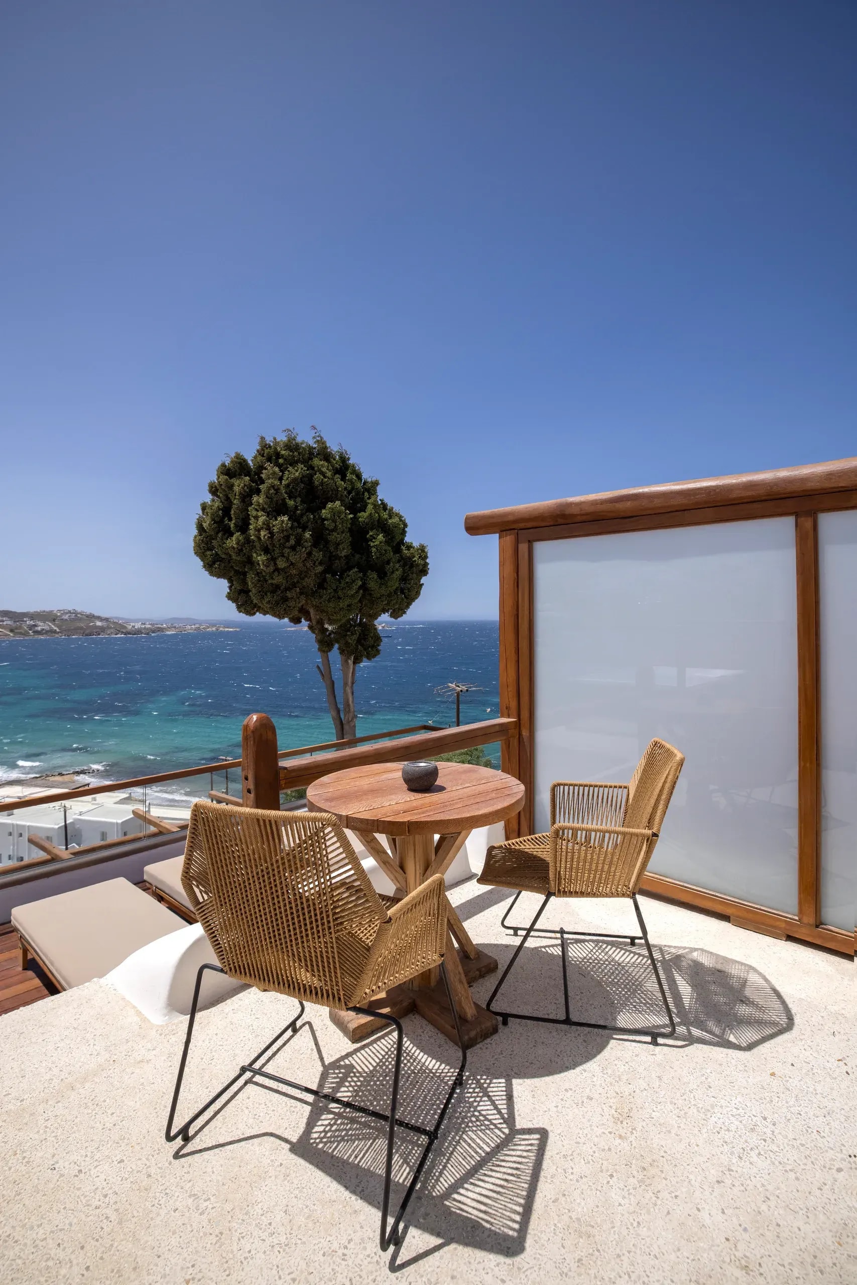 Table and chairs set on a private terrace, with a tree and the open sea beyond