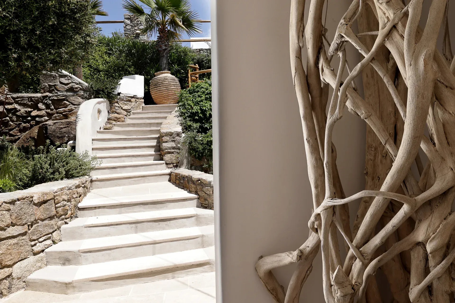 Whitewashed stone steps rising between planting, beside a driftwood sculpture